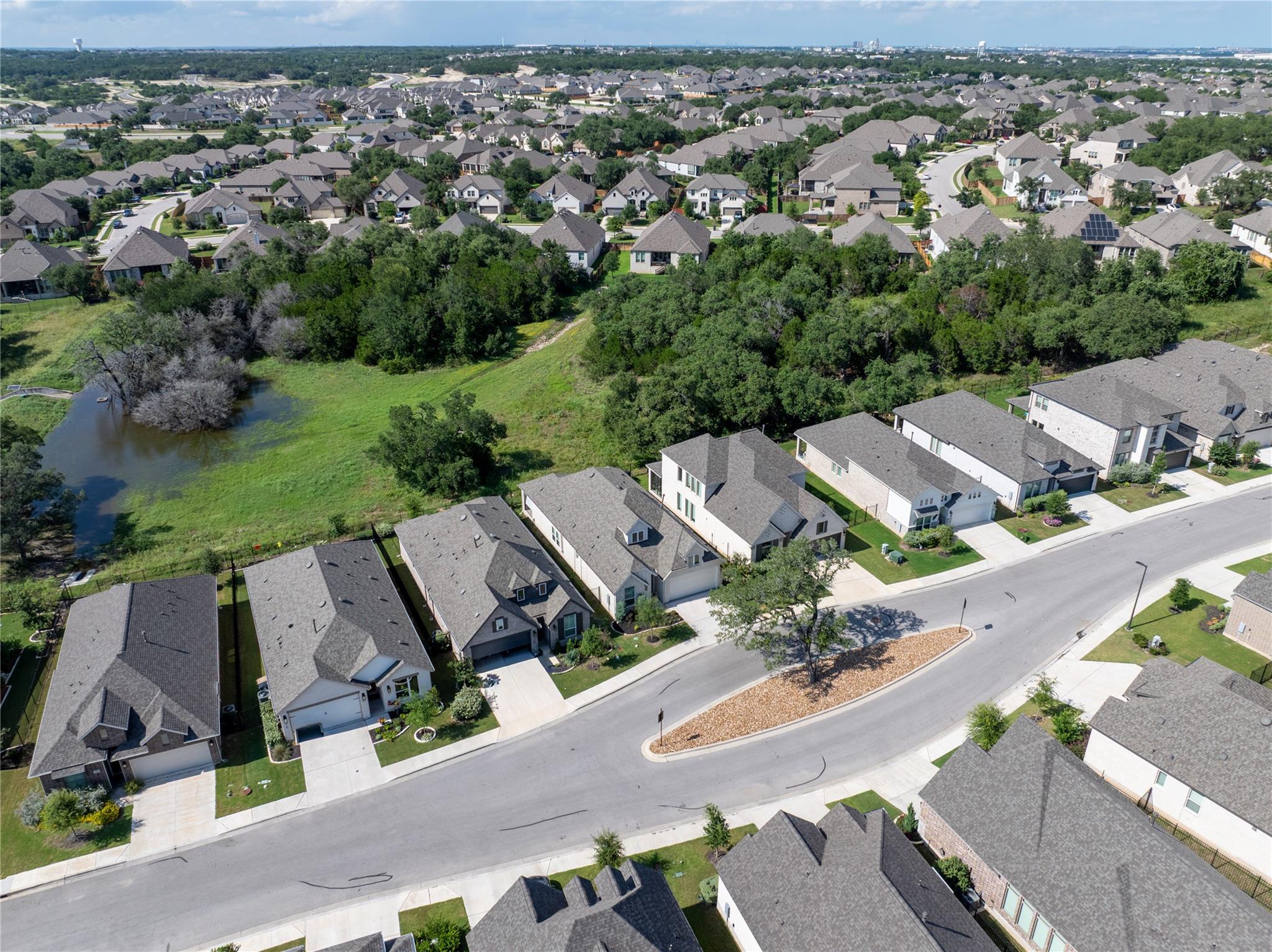 Aerial view of homes beside a wooded greenbelt and small pond.
