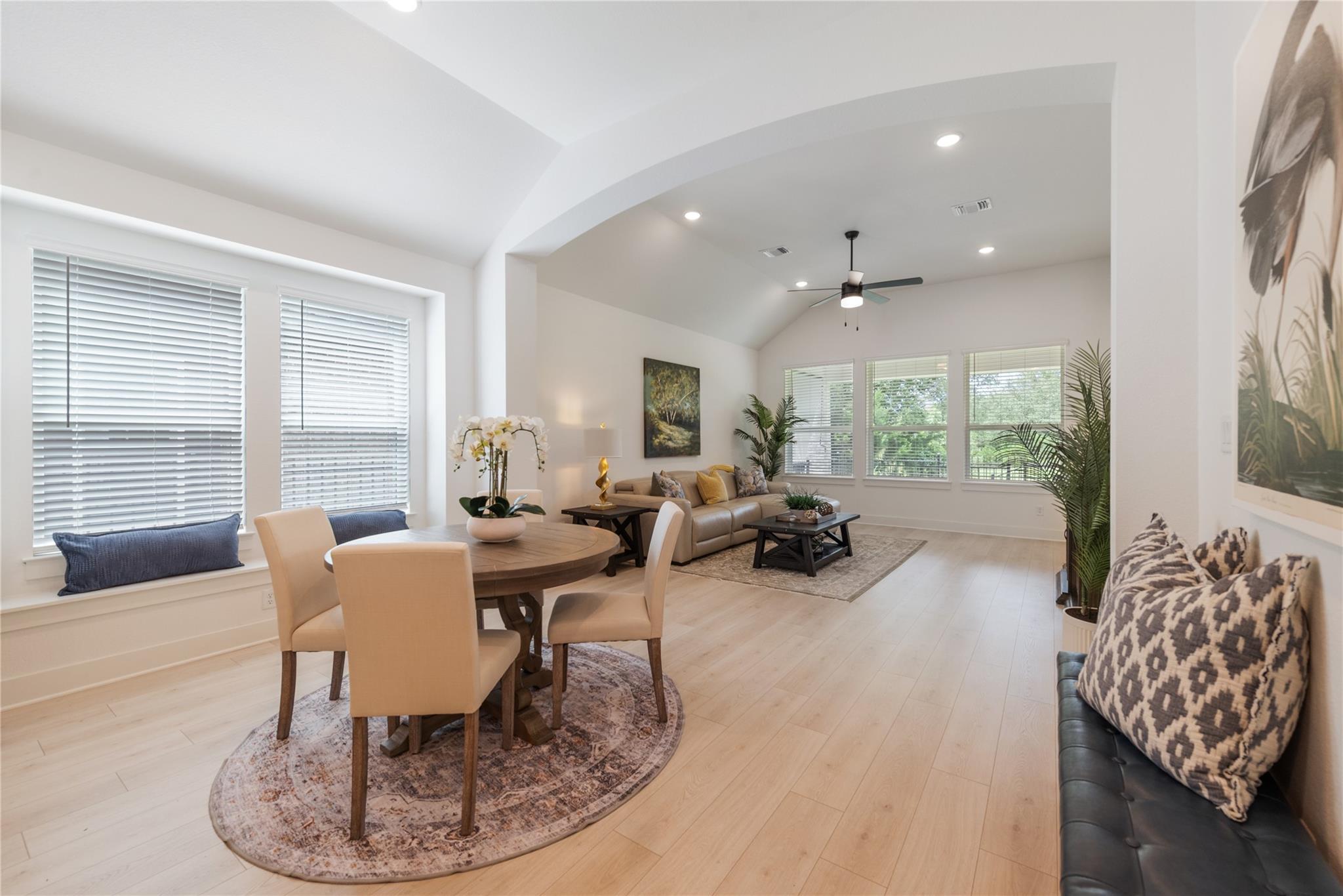 Open dining and living area with a vaulted ceiling, round dining table, and beige sofa.