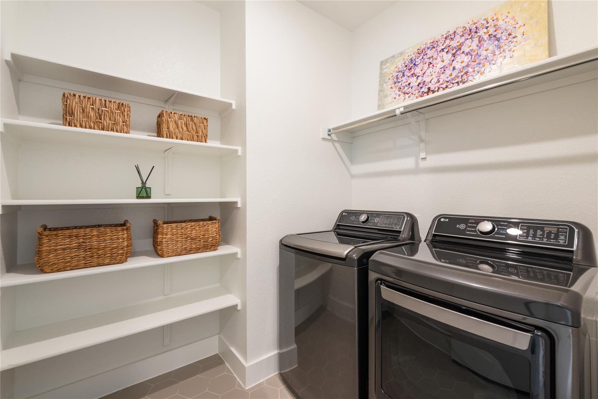 Laundry room with dark washer and dryer beside white shelves and woven baskets.