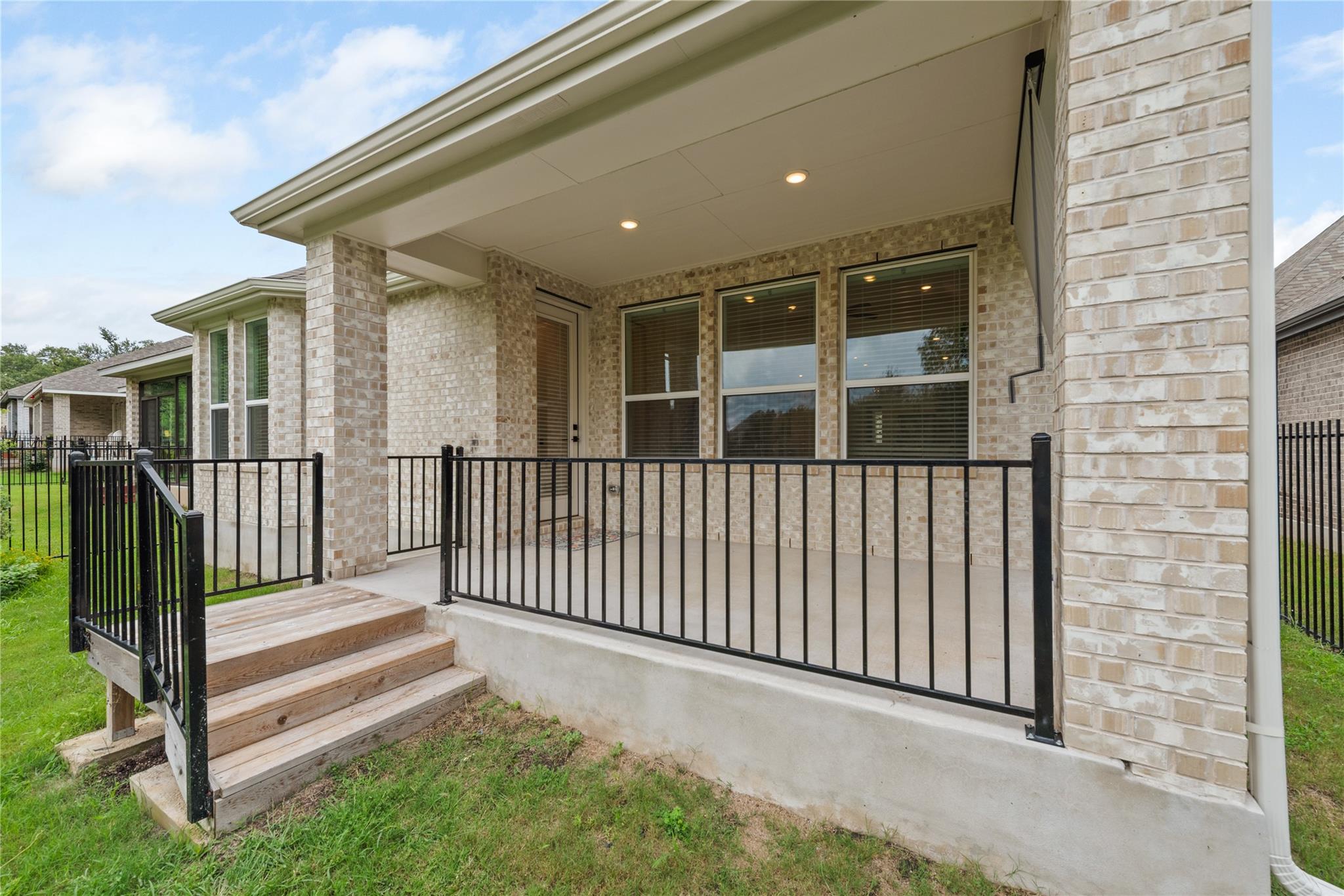 Covered rear porch with black metal railing, brick walls, and wooden steps leading to the lawn.