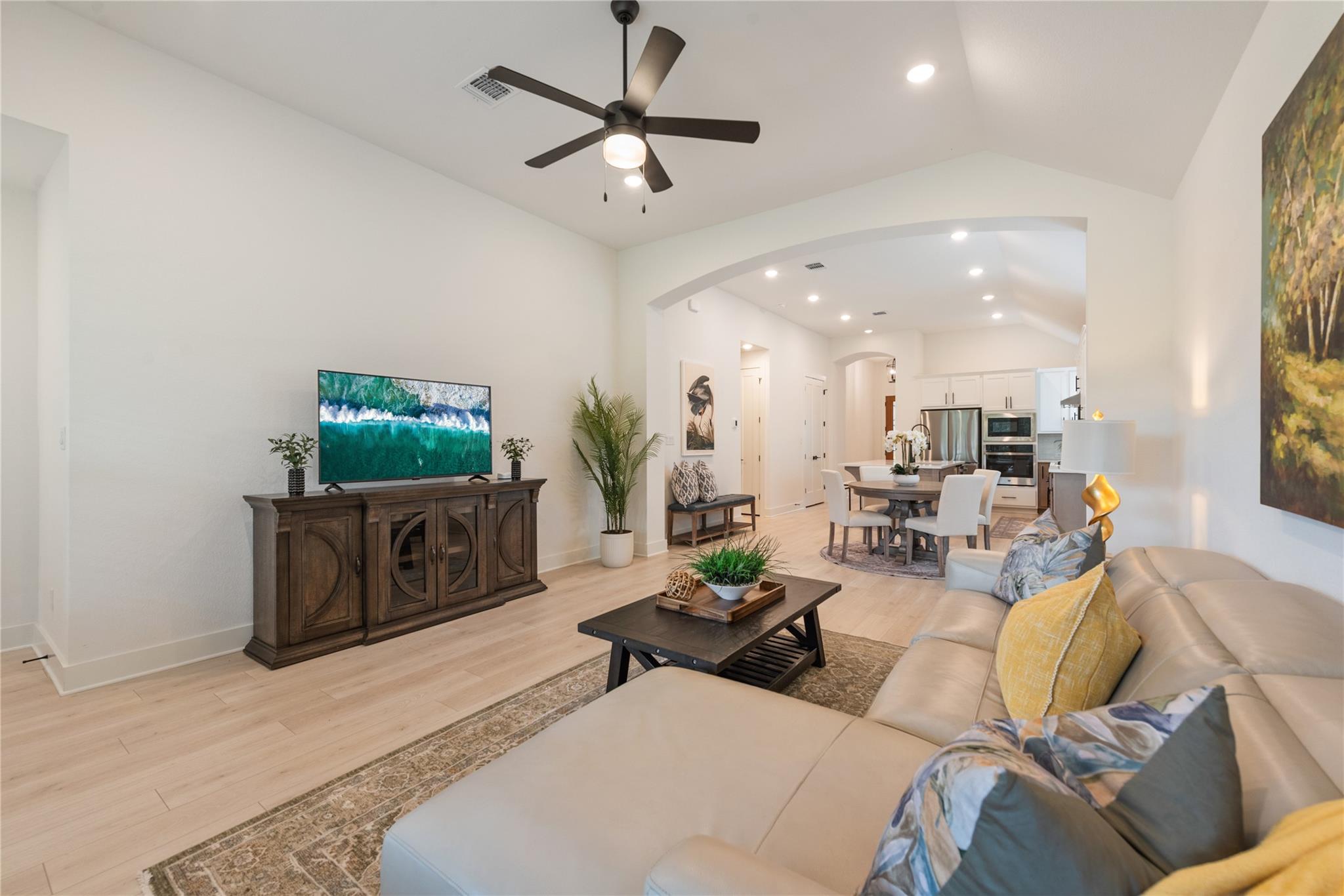 Living room with a ceiling fan, large sectional sofa, and open dining and kitchen area.