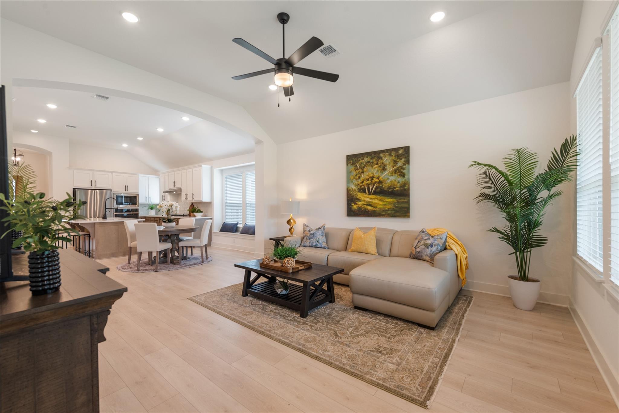 Open-plan living room and kitchen with a beige sectional, dining area, and ceiling fan.