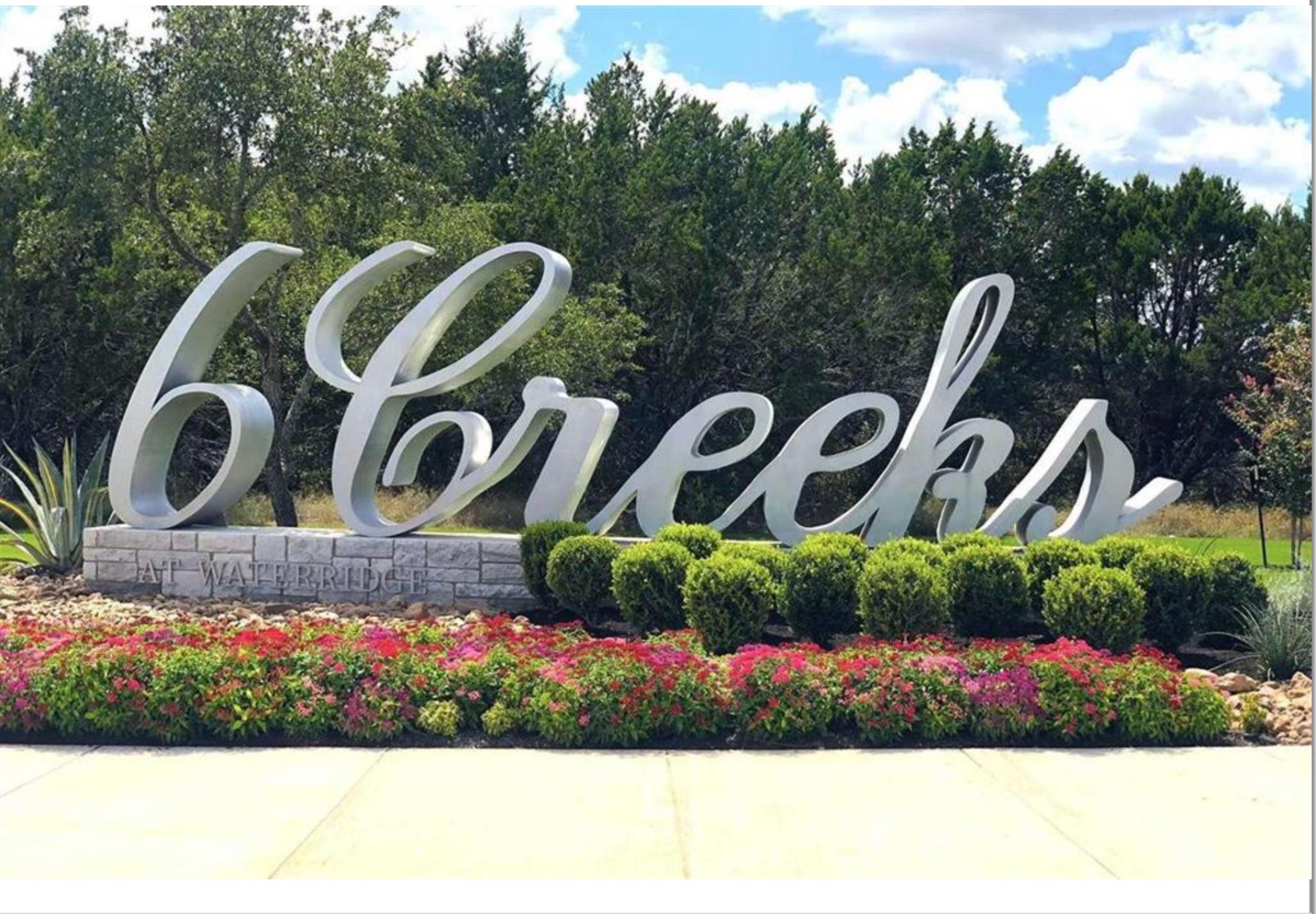 Community entrance sign reading “6 Creeks at Water Ridge,” set among flowering shrubs and trees.