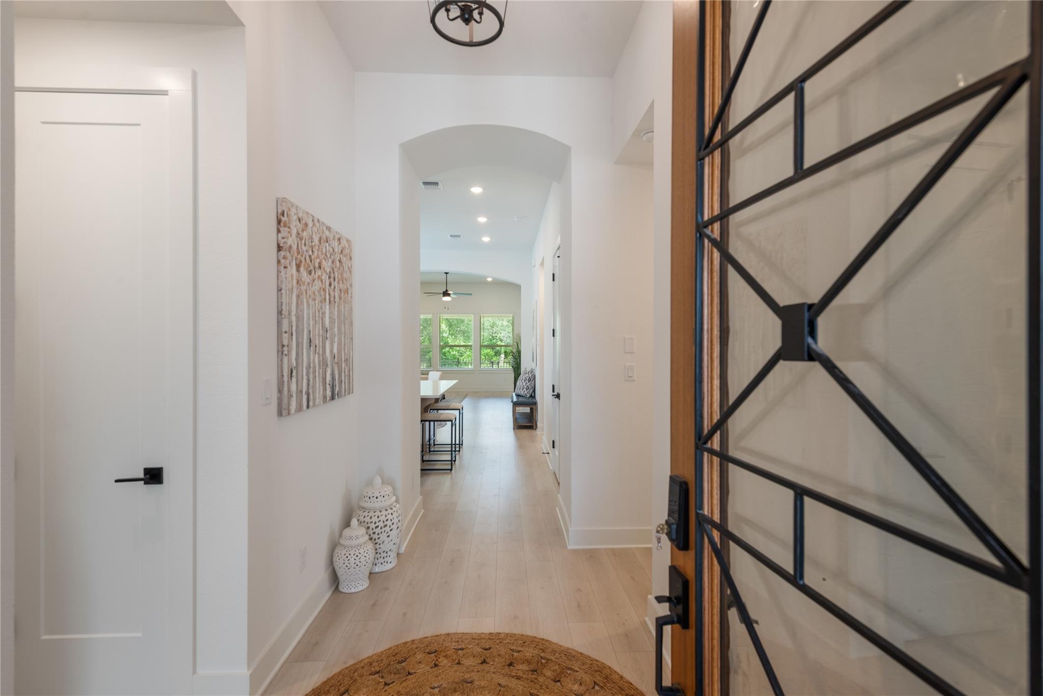 Entry hallway with a black geometric glass front door, light wood flooring, and an arched opening to the dining area.