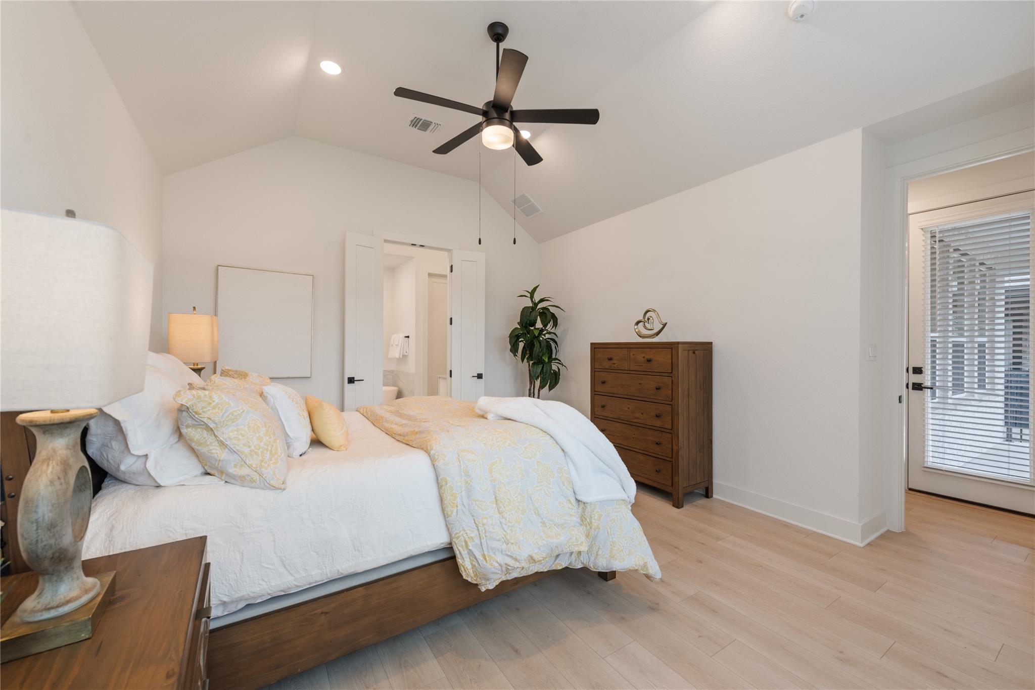 Bedroom with a vaulted ceiling, ceiling fan, and a wood dresser beside the bed.