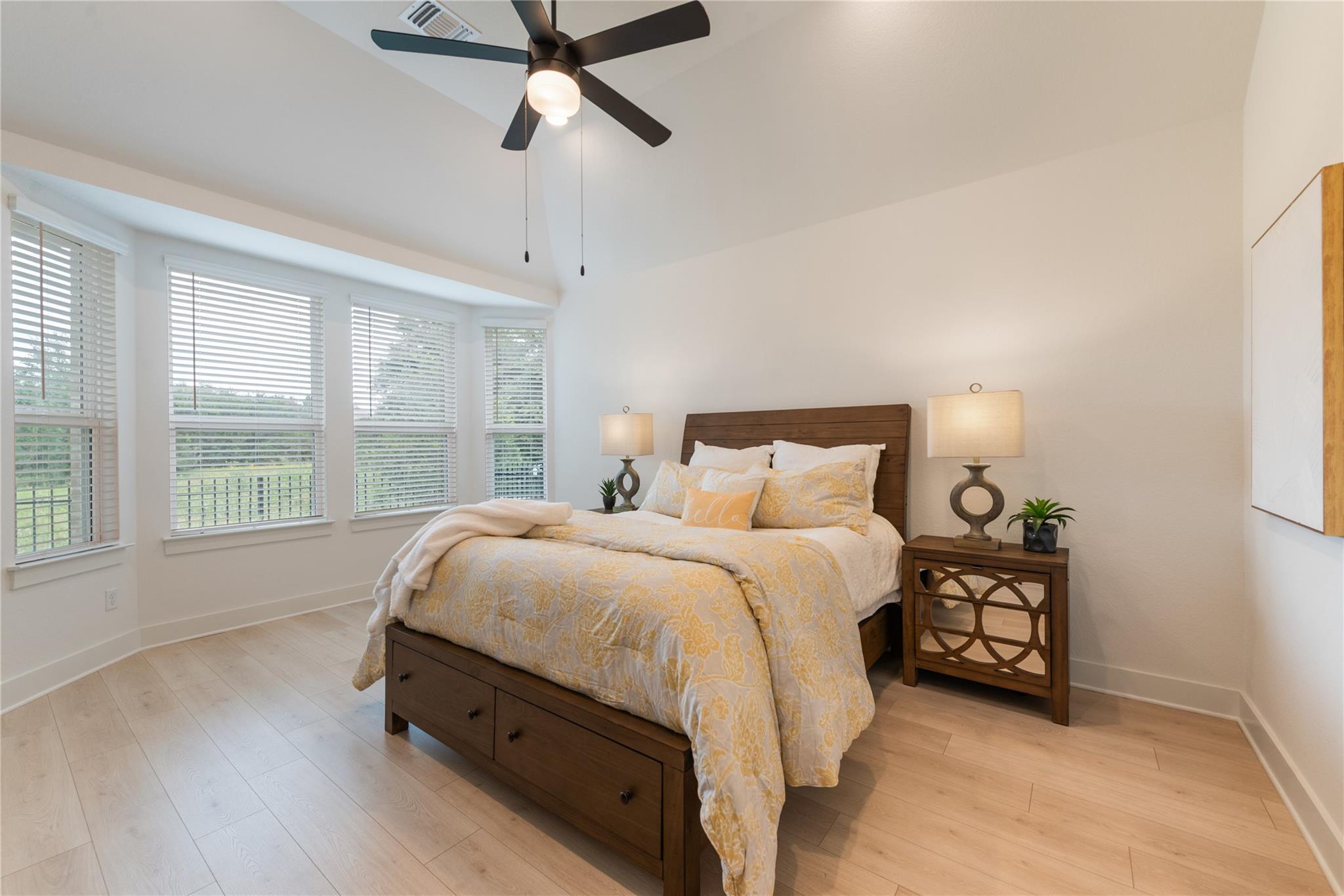 Staged bedroom with a dark wood bed, pale yellow bedding, and a curved wall of windows.