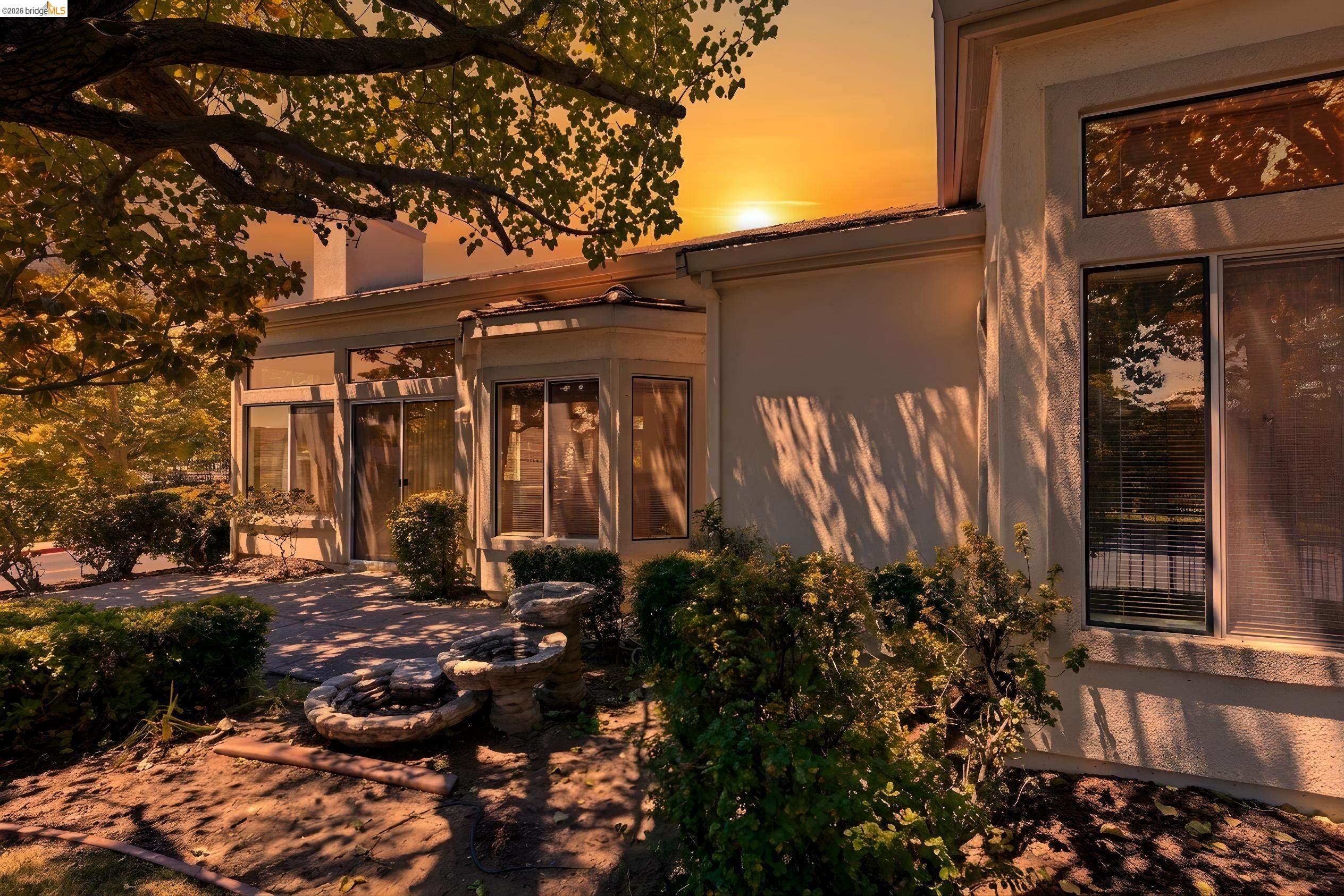 Modern home with a landscaped courtyard and tiered stone fountain at sunset.