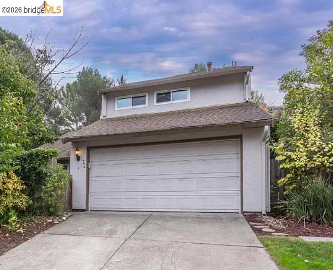 Gray two-story home with a wide white garage door, upper windows, and leafy landscaping.