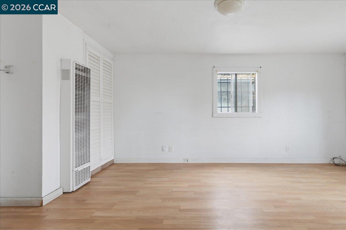 Vacant room with light wood flooring, a barred window, and a wall-mounted heater.