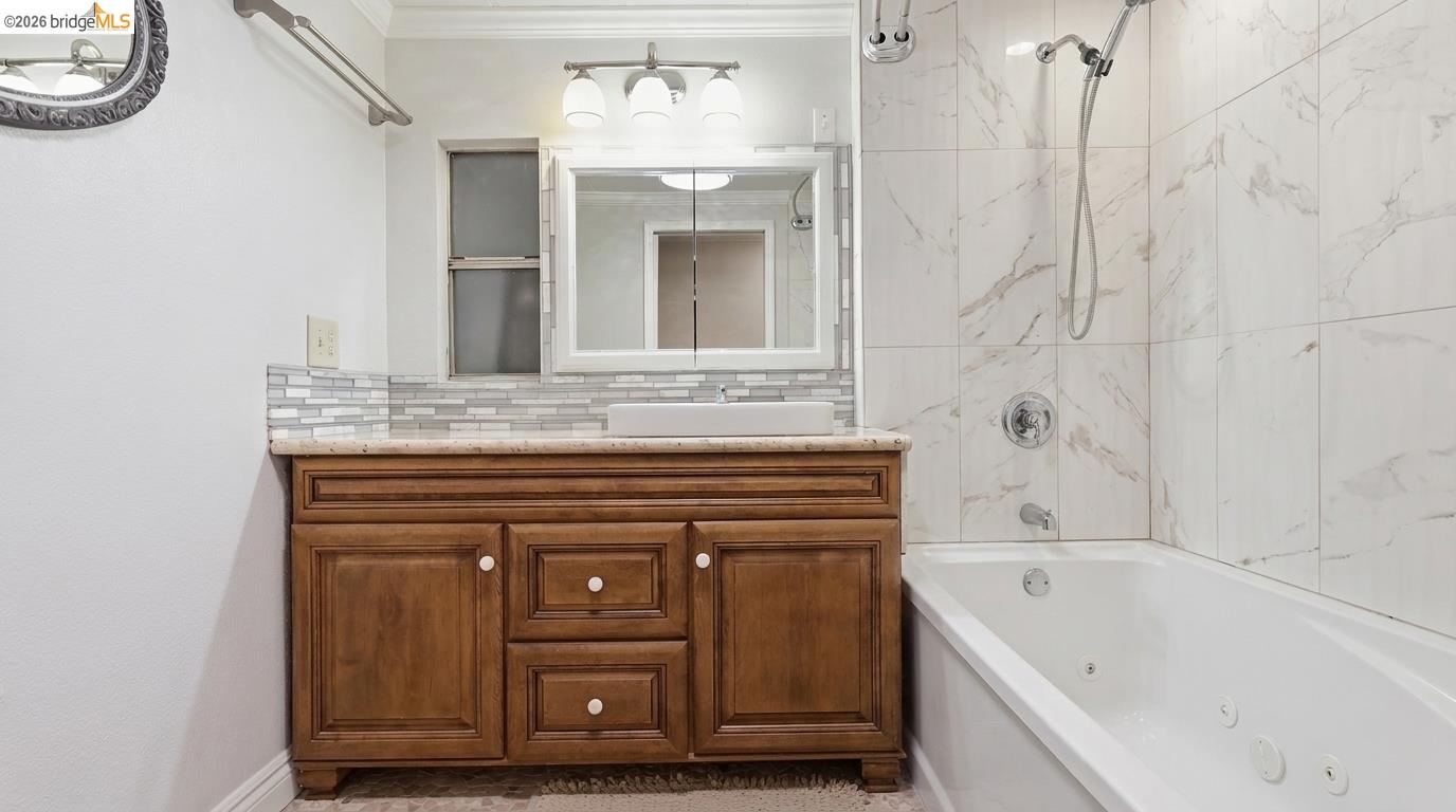 Bathroom vanity and bathtub with marble-look tile and a handheld shower.
