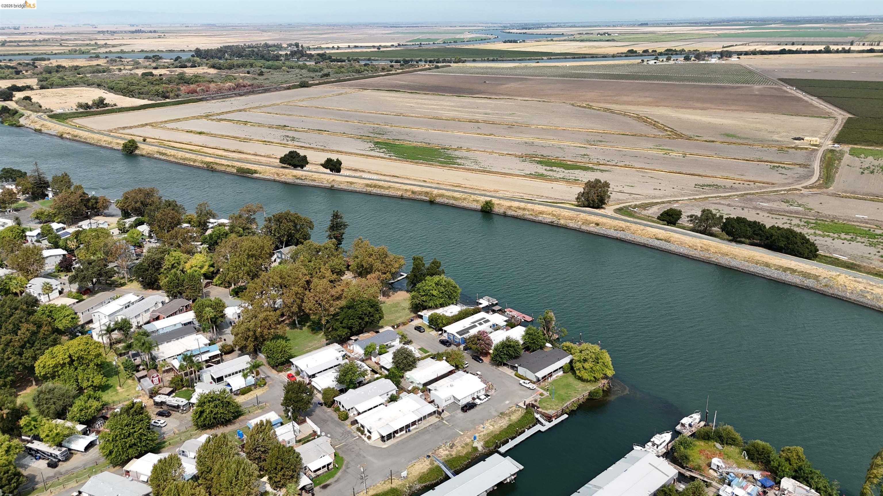 Aerial view of a canal-side community with docks and boats, across from expansive farmland.
