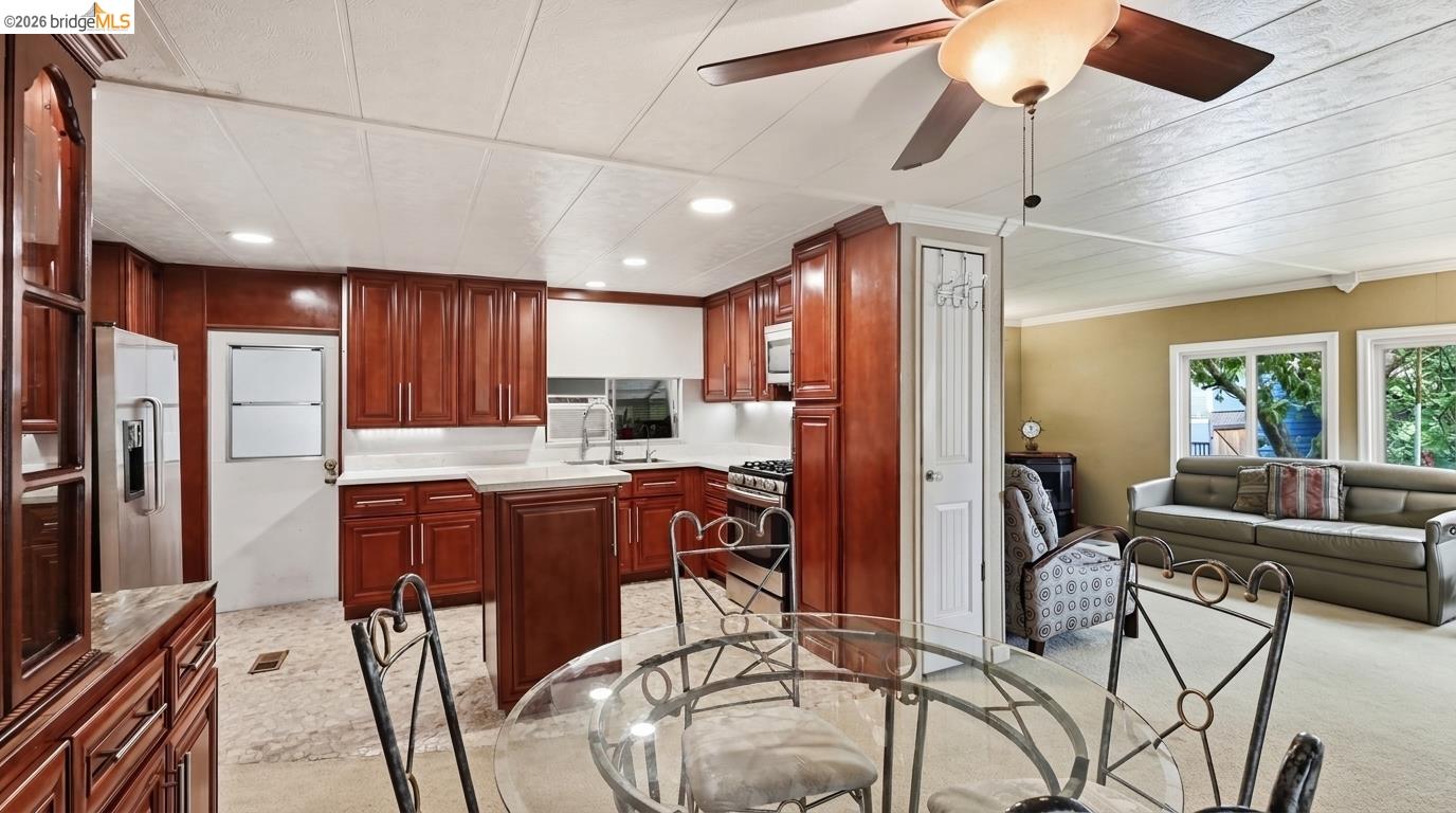 Kitchen with reddish-brown cabinets and glass dining table opening onto a living room with gray sofa.