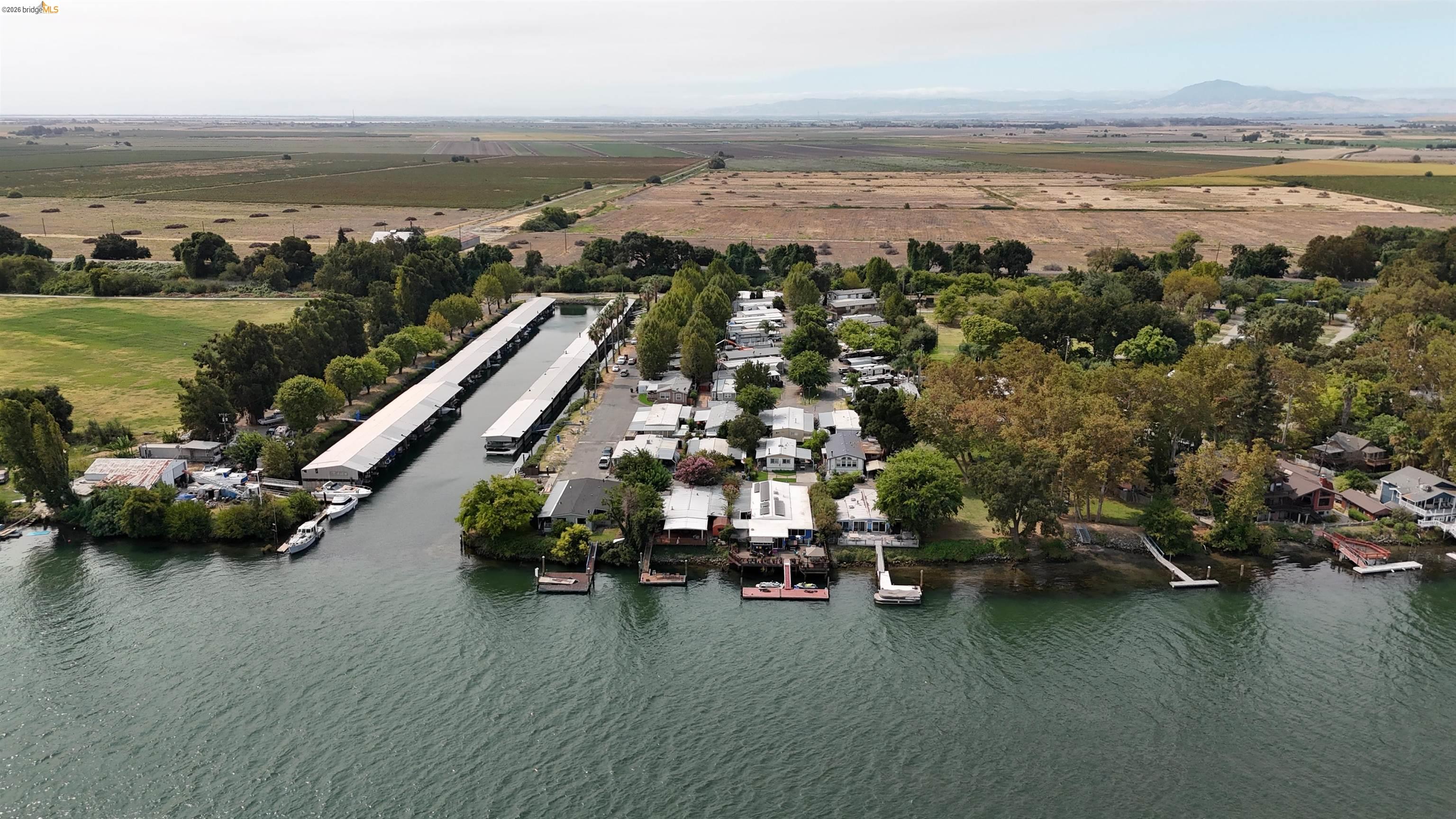 Aerial view of waterfront homes and docks along a canal, with farmland and distant mountains beyond.