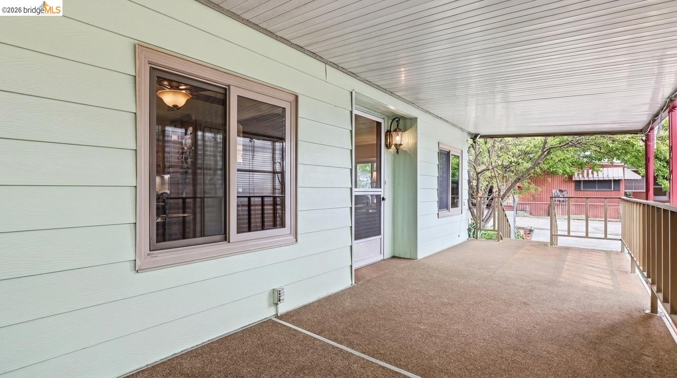 Covered porch with pale mint siding, large windows, and a railing overlooking leafy trees.