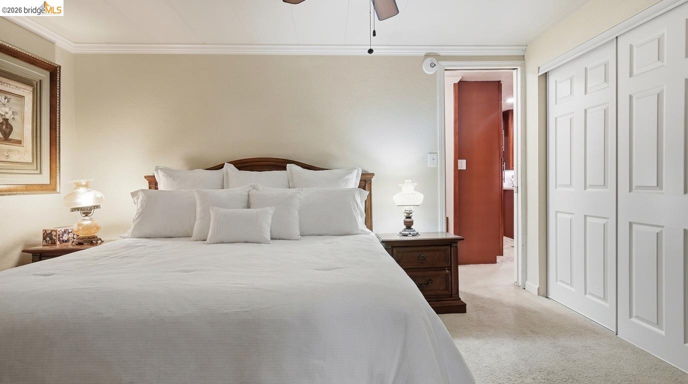 Furnished bedroom with a large white bed, dark wood headboard, and white closet doors.