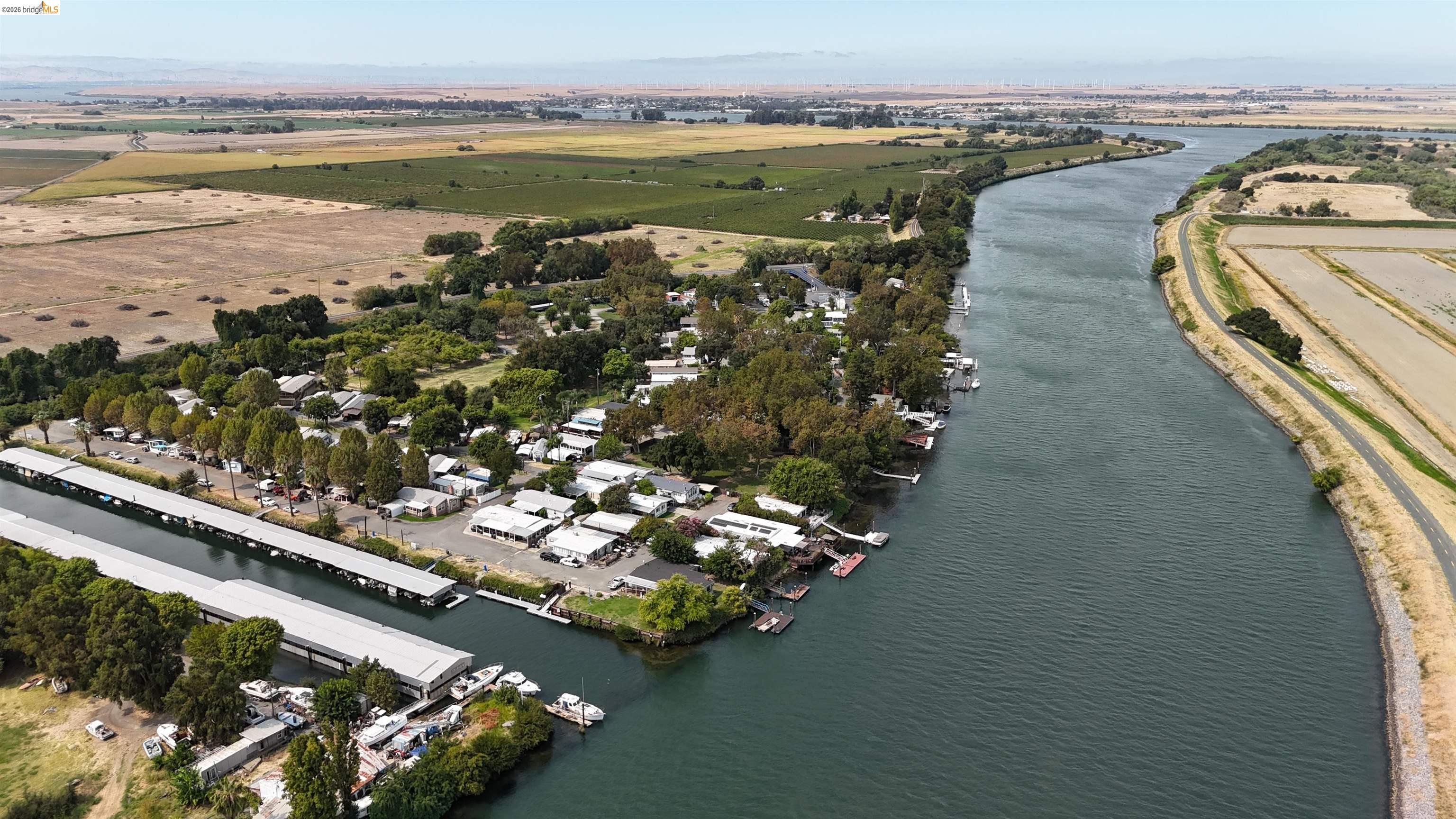 Aerial view of riverfront homes and boat docks beside a broad river and surrounding farmland.