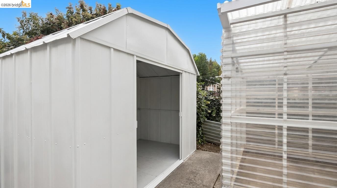 White metal storage shed with its sliding door open beside a translucent covered structure.