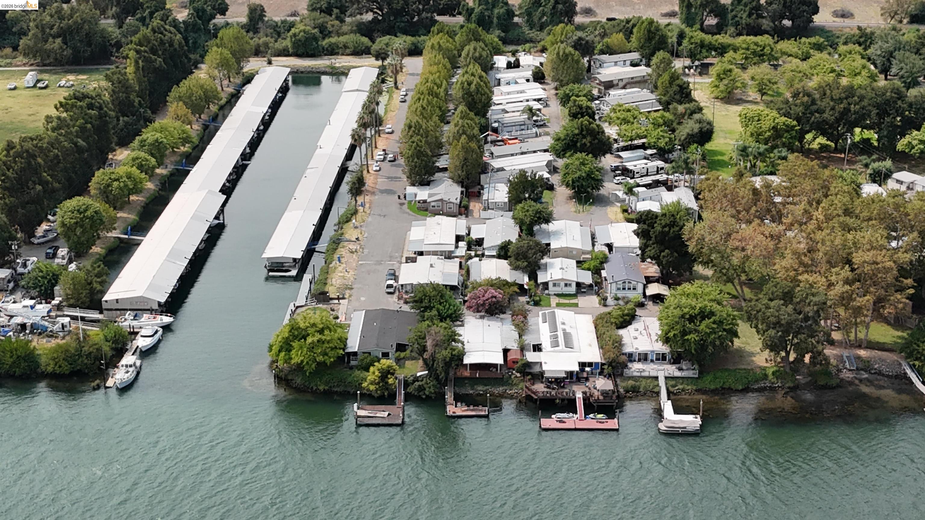 Waterfront homes and private docks beside a broad waterway, with covered marina slips nearby.