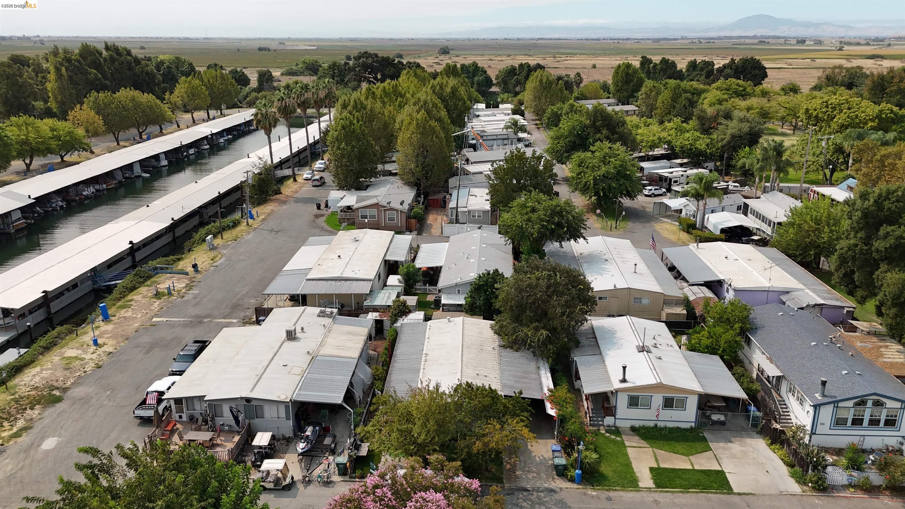 Aerial view of homes beside a canal with covered boat slips and open fields beyond.