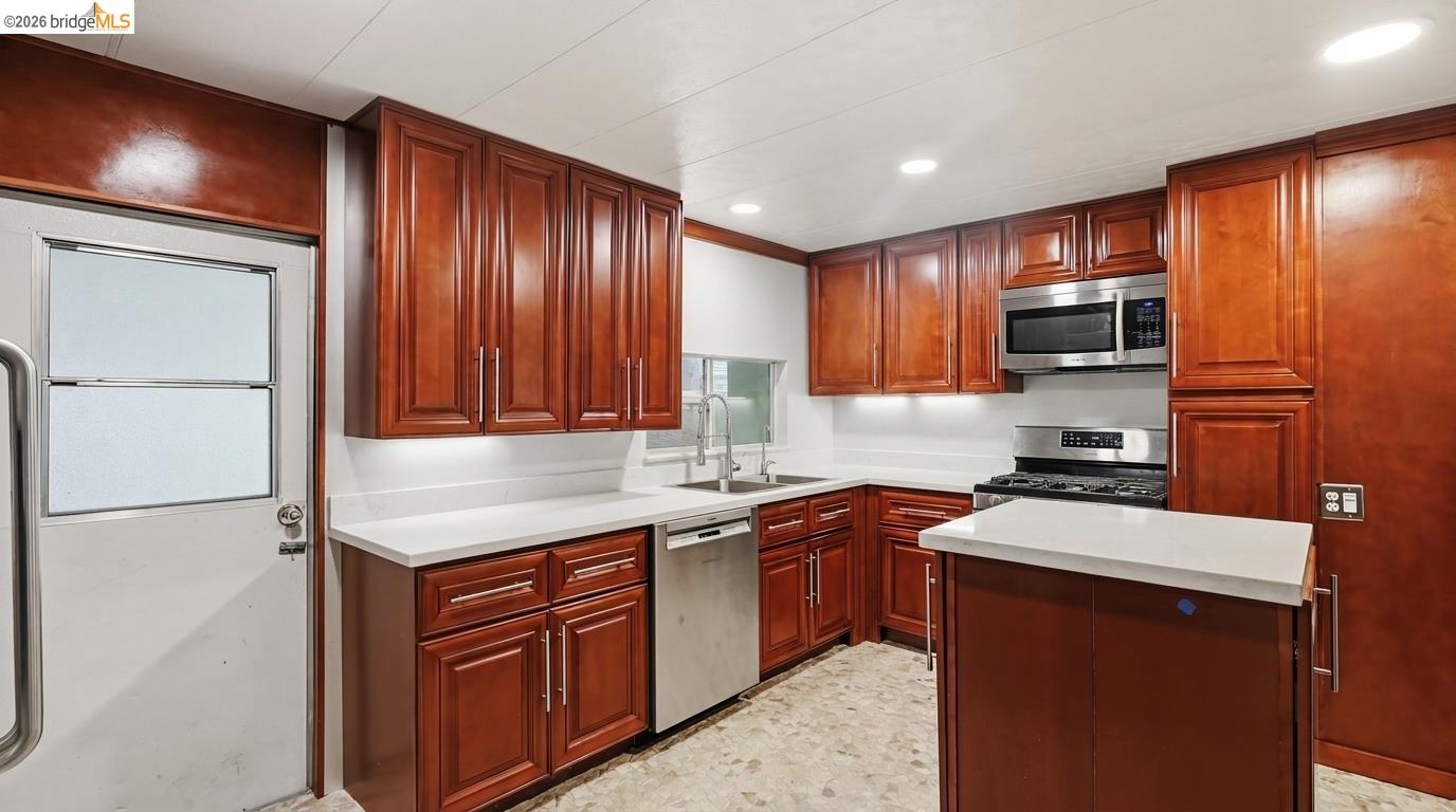 Kitchen with reddish wood cabinets, white counters, a central island, and stainless steel appliances.