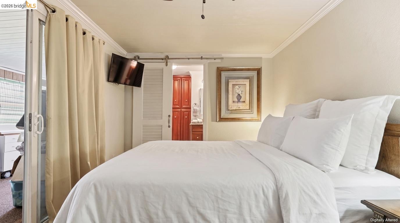 Bedroom with a white bed, cream curtains, wall-mounted TV, and bathroom doorway with red cabinetry.