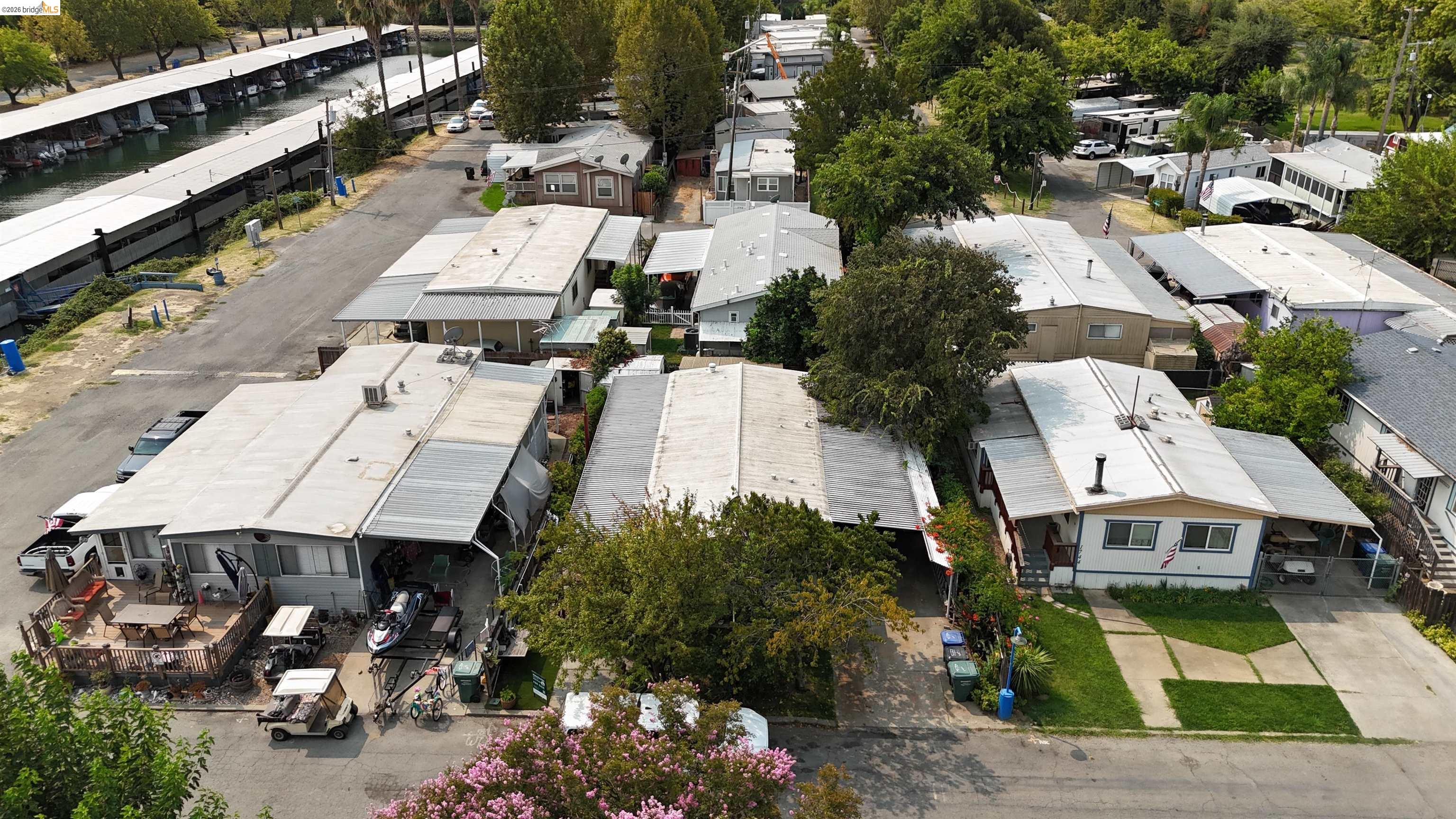 Aerial view of a manufactured-home community beside a marina, with covered boat slips and tree-lined lanes.