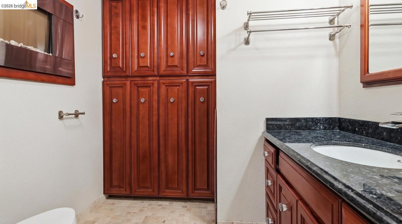 Bathroom with paneled wood cabinets, a black stone vanity, and an oval sink.