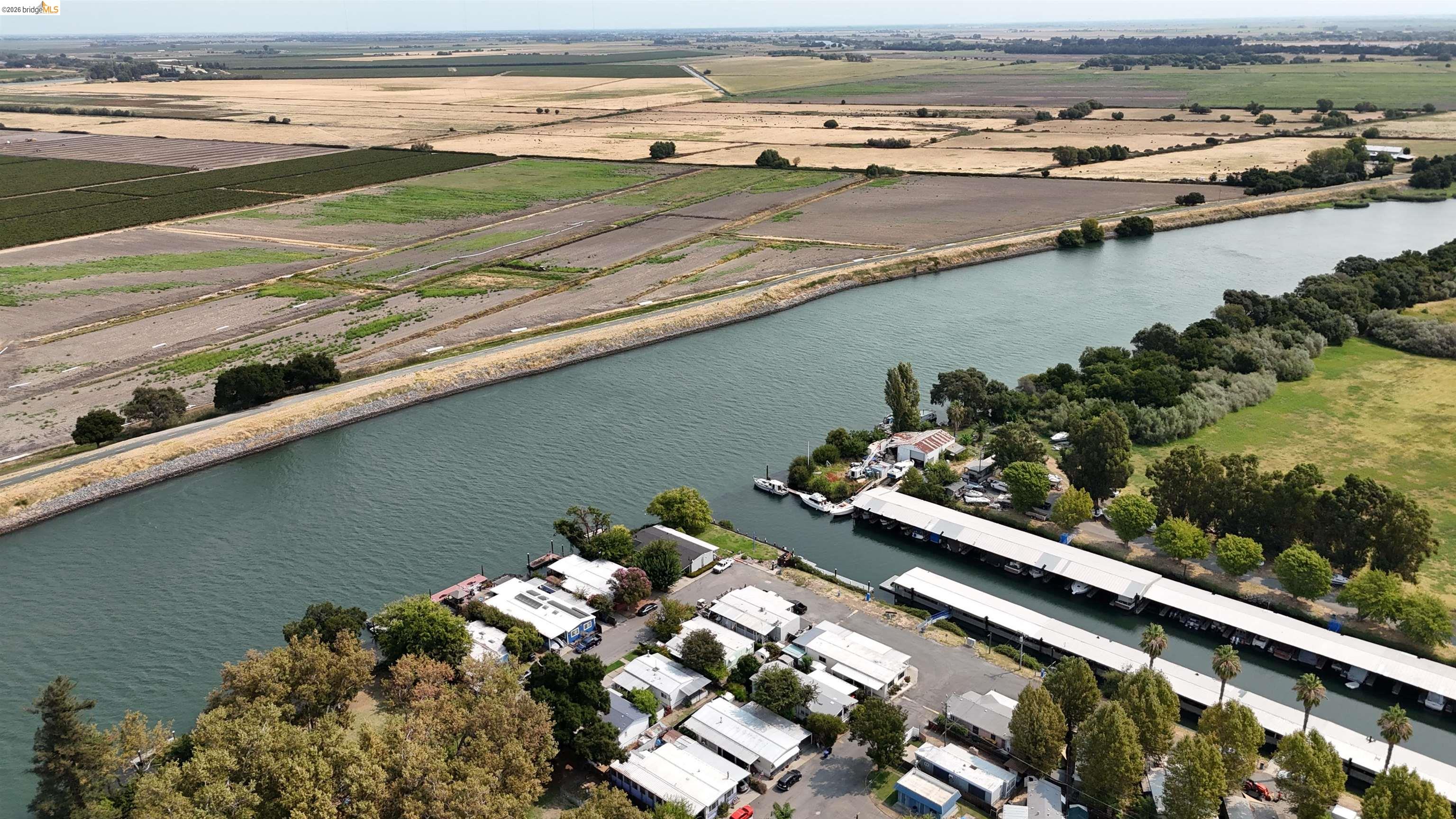 Aerial view of a riverfront community with covered boat docks and agricultural fields across the river.