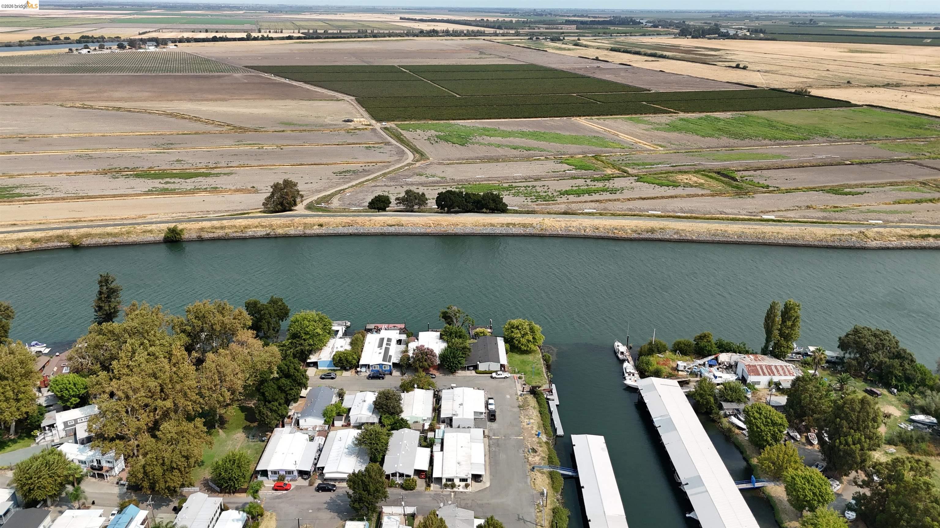 Aerial view of homes along a canal, with covered docks and farmland beyond.