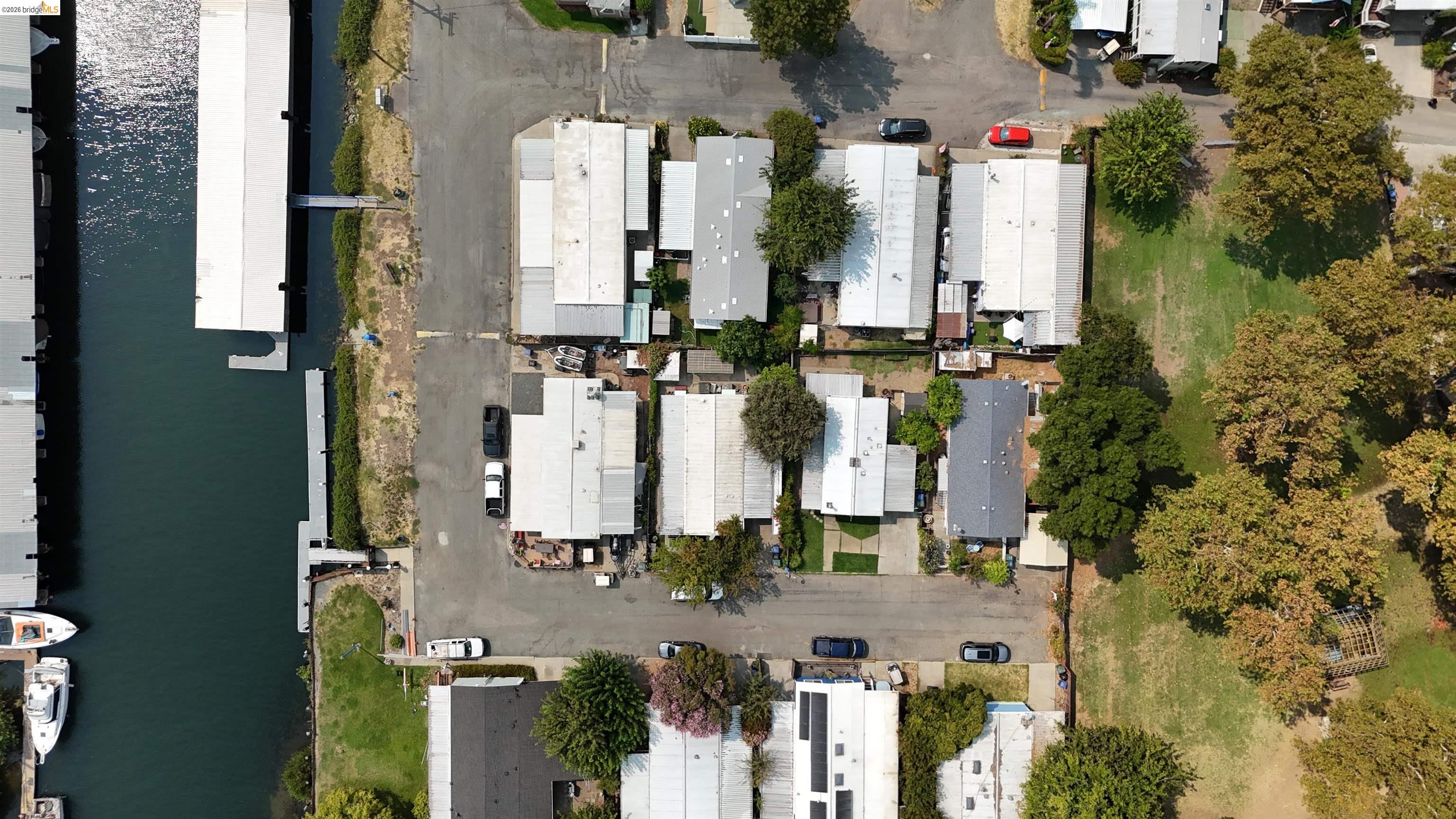 Aerial view of waterfront homes beside a marina channel, with boat docks and a tree-lined grassy area.