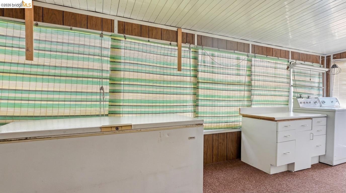 Laundry room with a chest freezer, washer and dryer, and striped blinds.