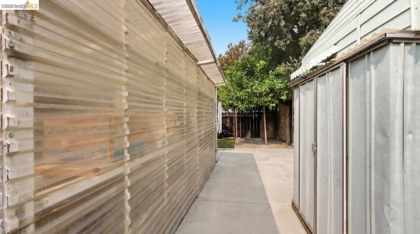 Concrete side yard between the home’s translucent-sided wall and screened sliding doors, ending at a shaded fence.
