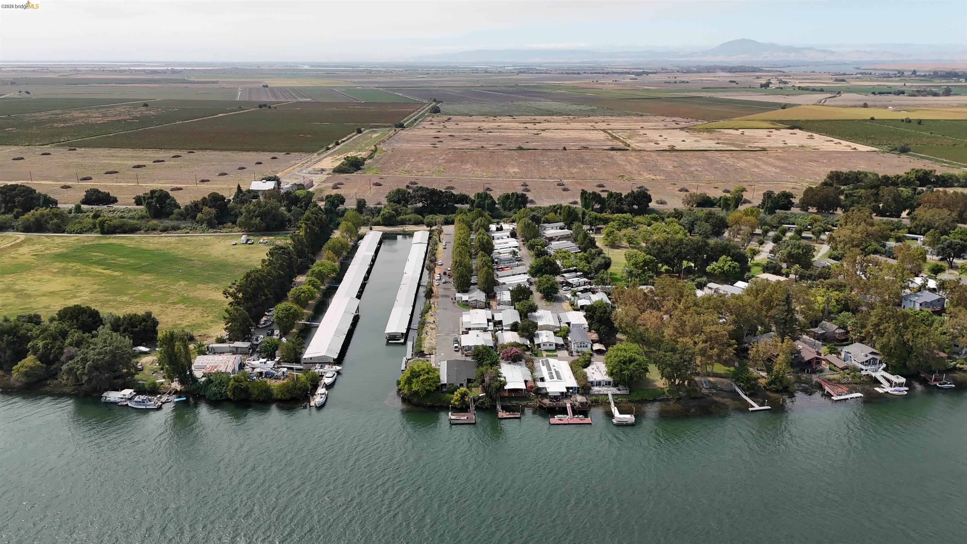 Aerial view of waterfront homes and docks beside a river, with farmland and distant mountains.