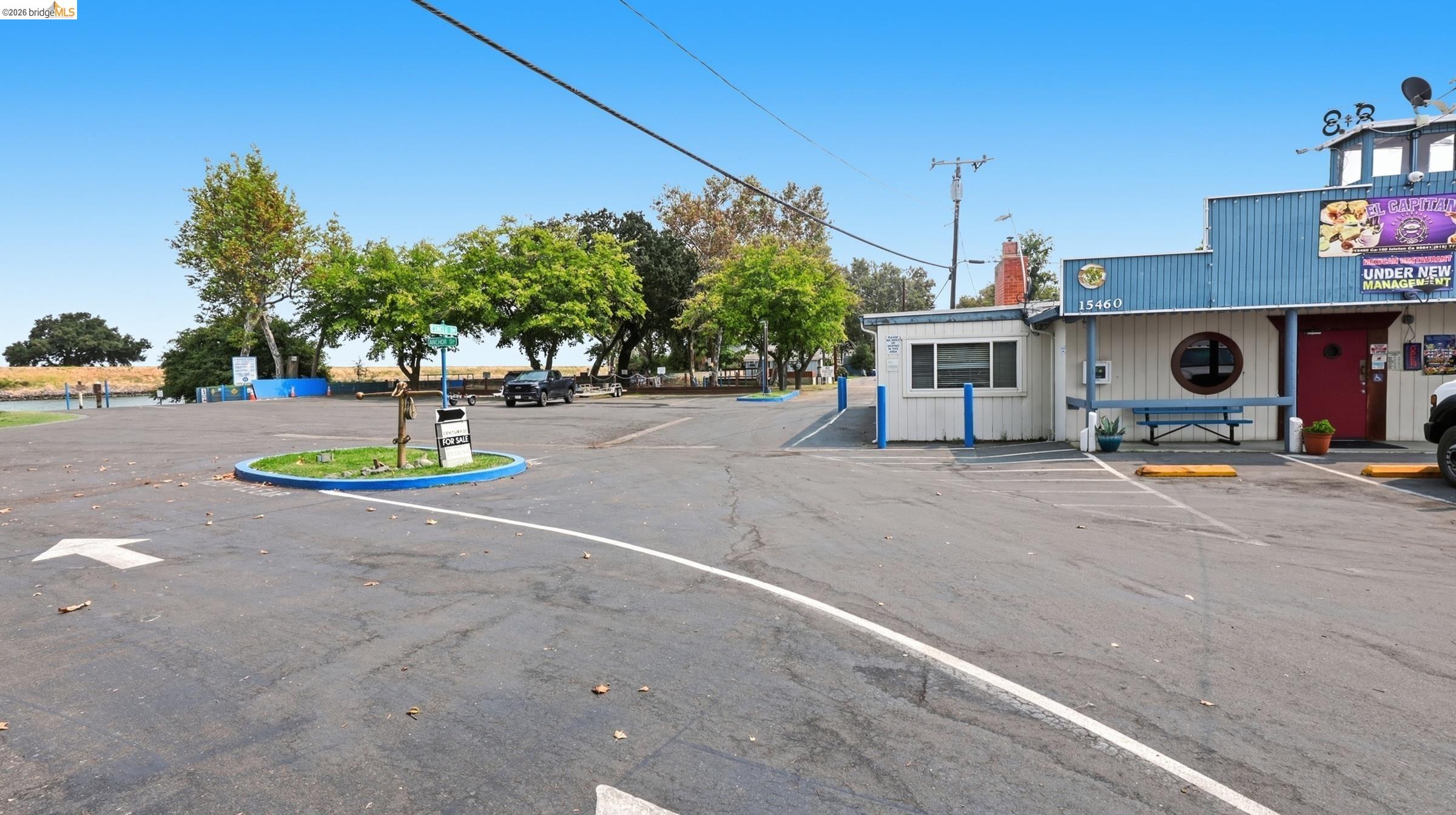 Commercial building exterior beside a waterfront parking lot, with a blue facade and a for-sale sign.