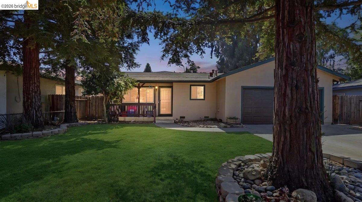 Single-story house with a front porch and garage behind a lawn framed by large trees.