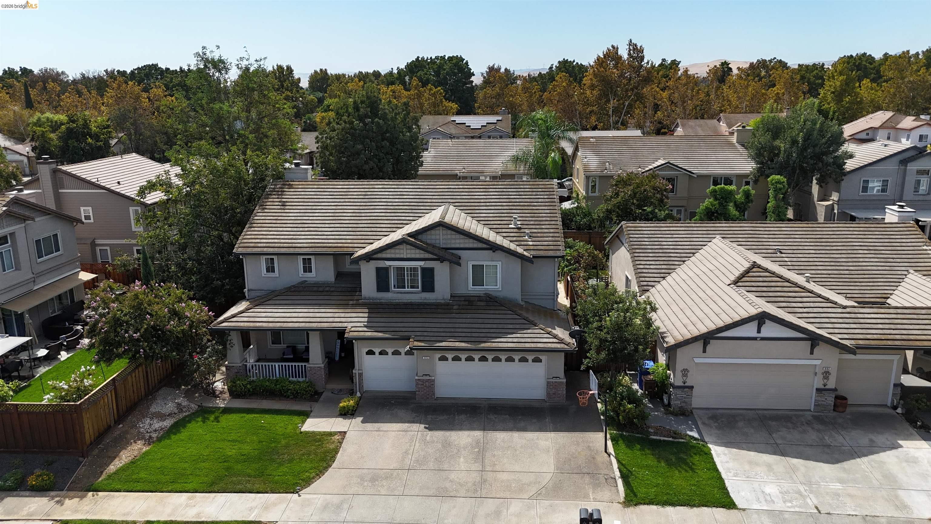 Aerial view of a gray two-story house with a tiled roof, attached garage, and green front lawn.