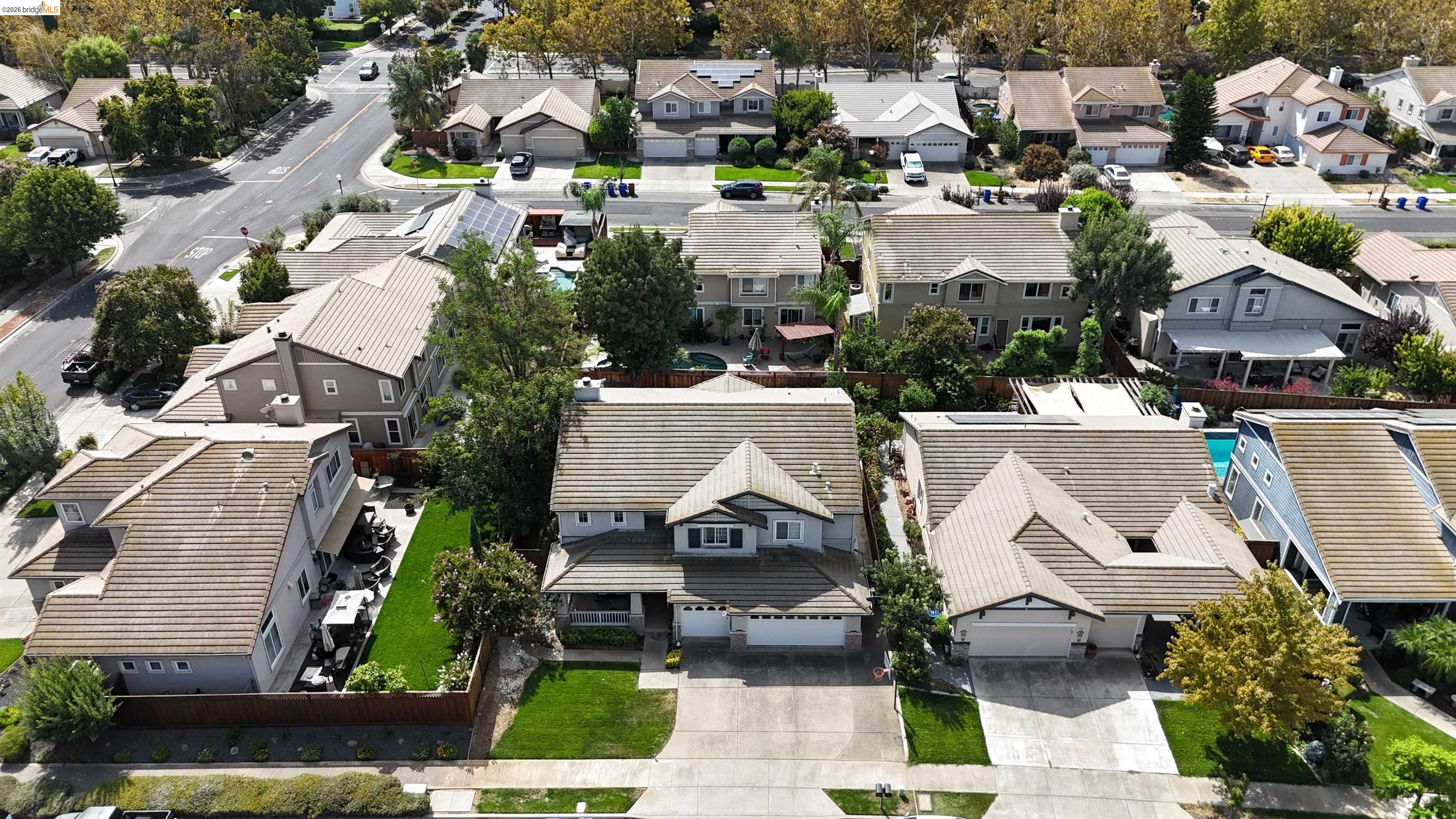 Aerial view of a suburban home with a tiled roof, front lawn, and neighboring houses.