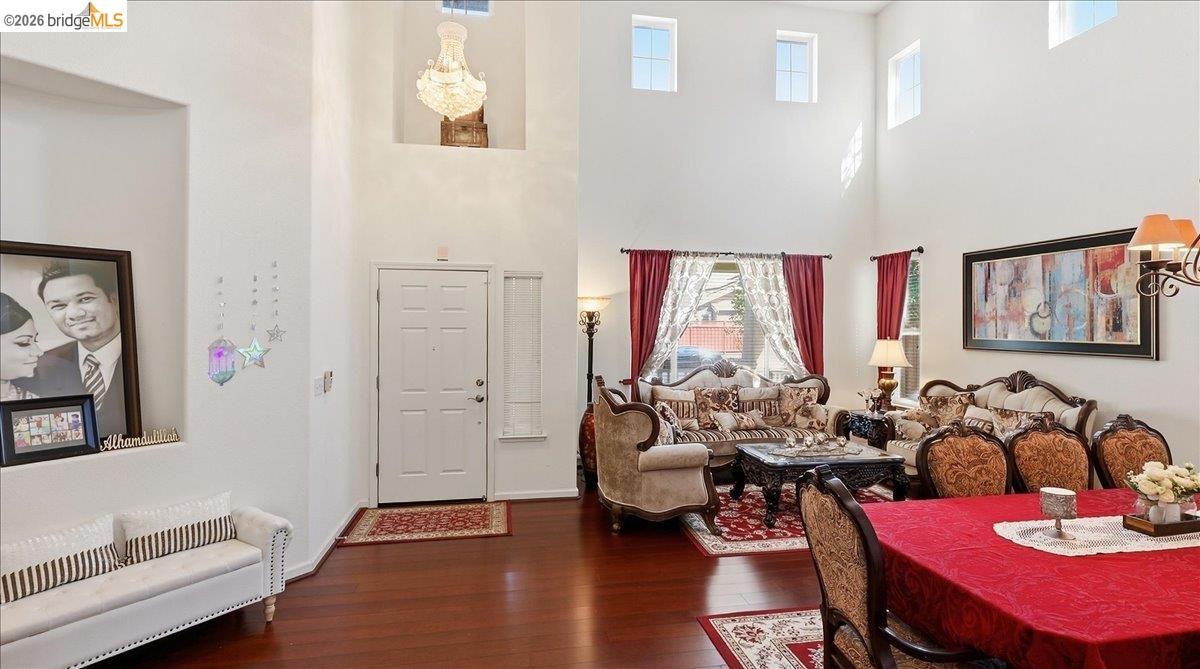 Double-height living and dining room with tall windows, ornate seating, and a red dining table.