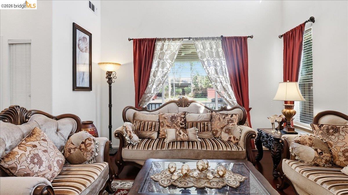 Living room with ornate upholstered seating, a glass coffee table, and red curtains.