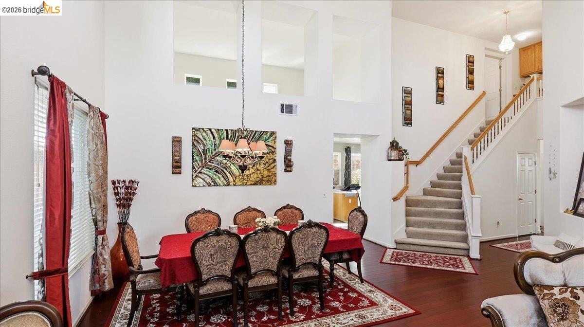 Dining room with ornate chairs and a red tablecloth beside a carpeted staircase.