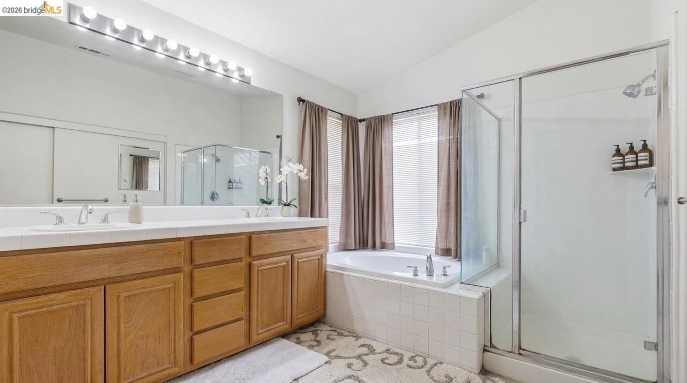 Bathroom with a long wood double-sink vanity, tiled bathtub, and glass-enclosed shower.