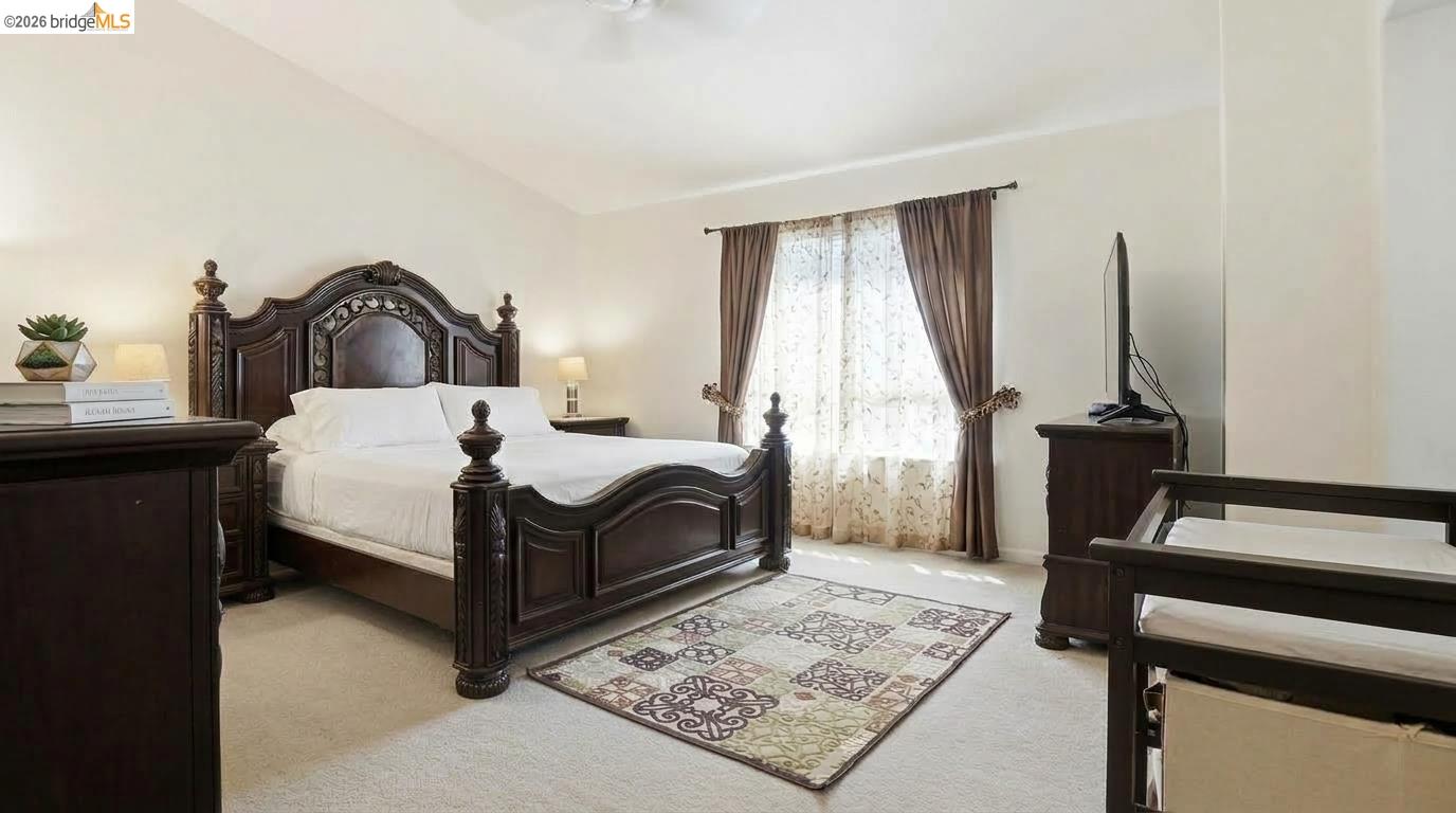 Bedroom with an ornate dark wood bed, patterned rug, and bright curtained window.