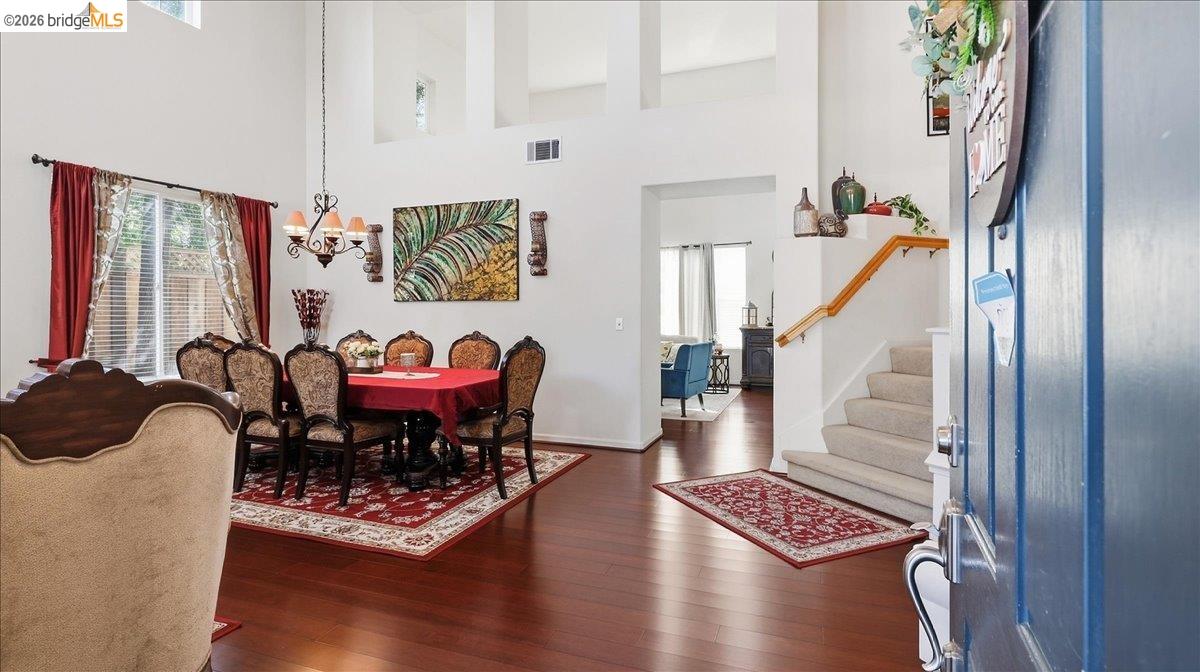 Formal dining room with ornate chairs and red tablecloth beside a staircase and open blue front door.