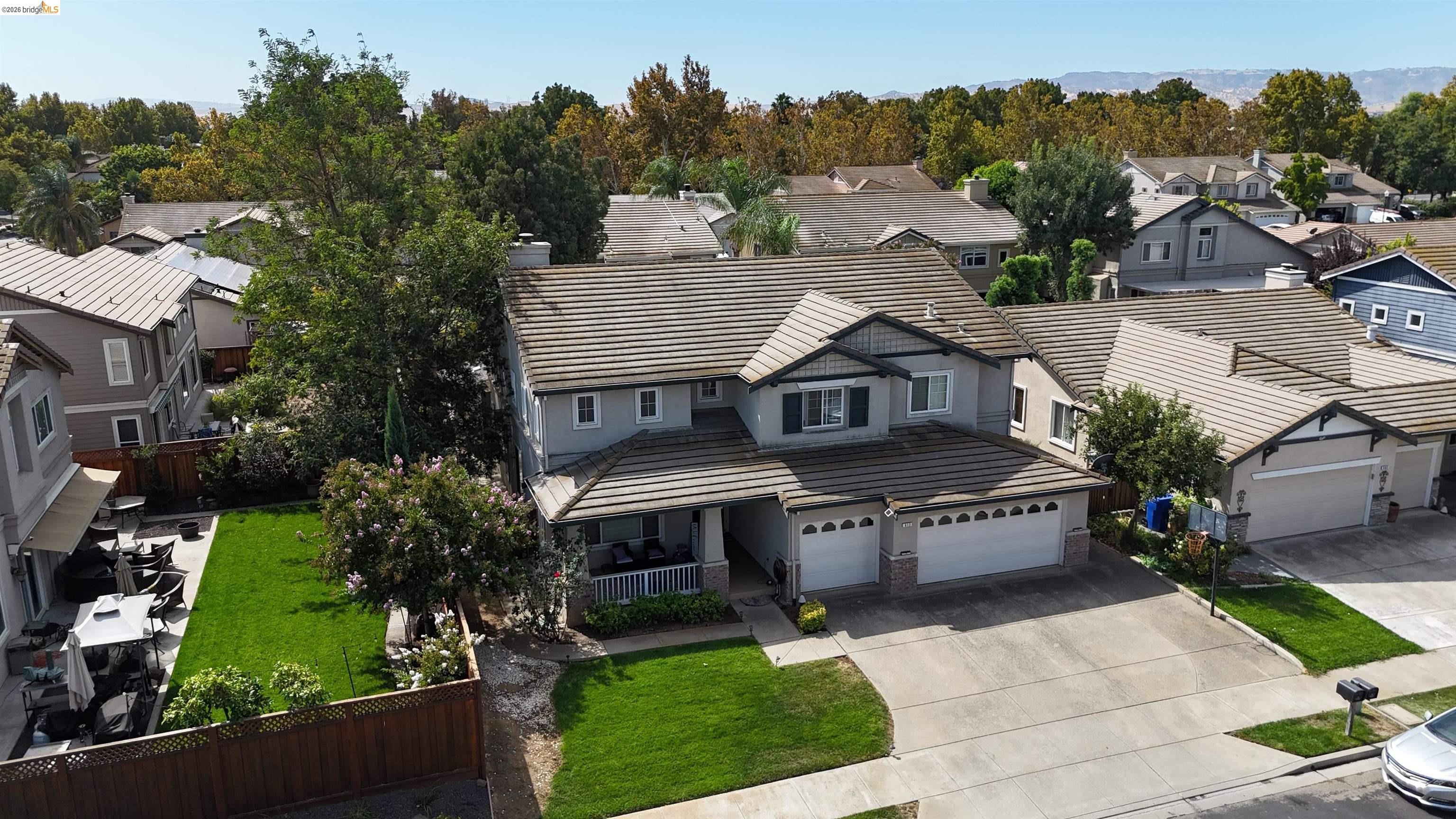 Aerial view of a gray two-story home with a tiled roof, two-car garage, and landscaped front lawn.