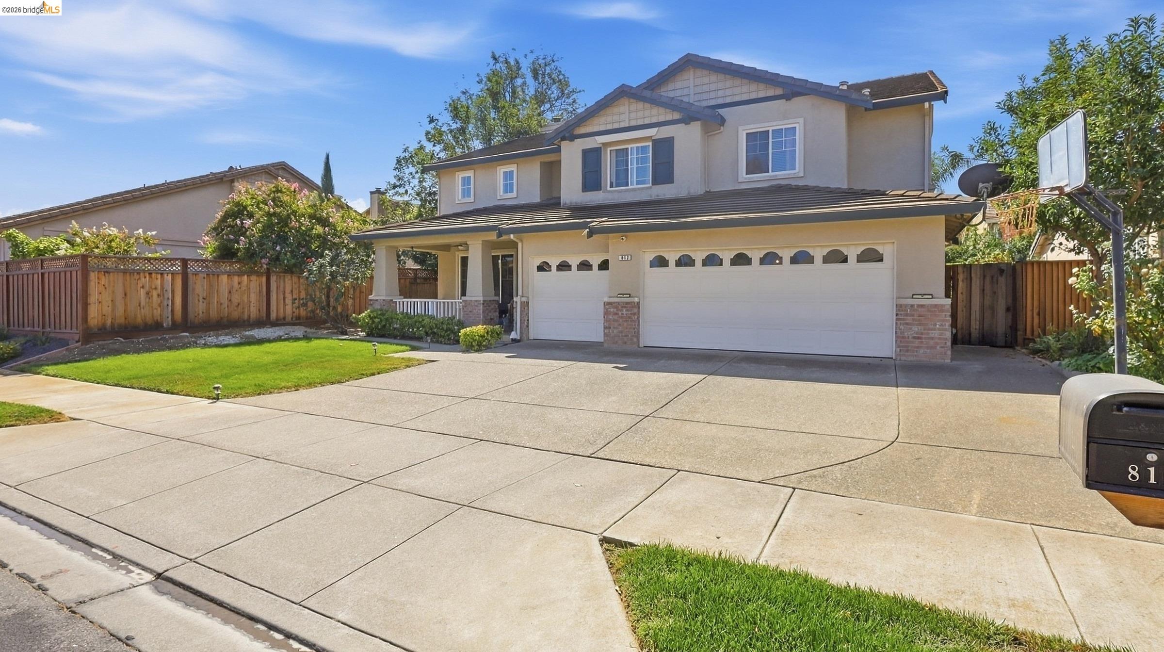Two-story beige home with a double garage, broad driveway, lawn, and basketball hoop.