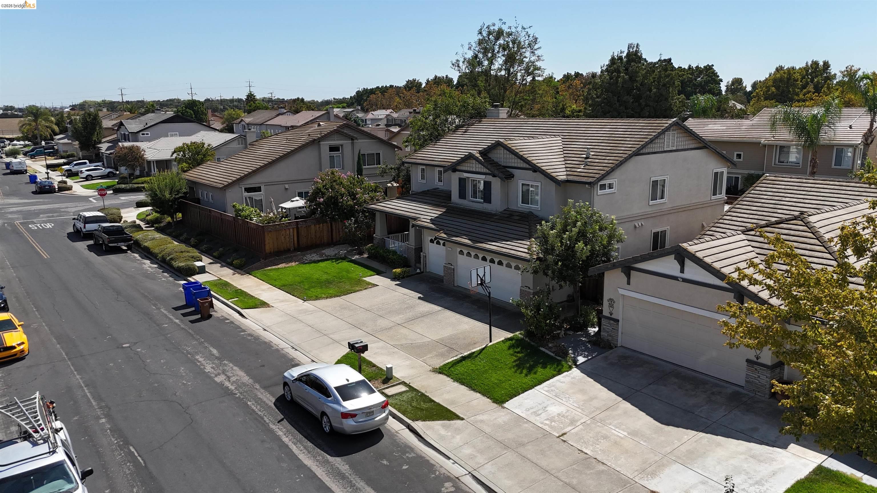 Gray home with a tiled roof, front lawn, wide driveway, and basketball hoop, viewed from above.