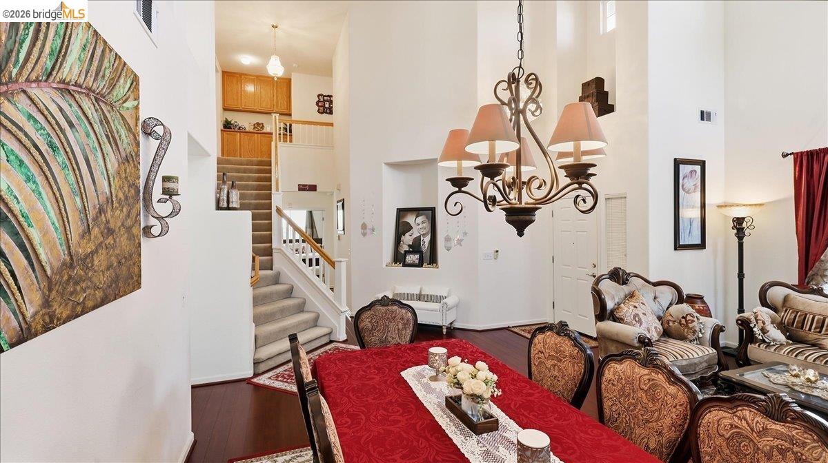 Open living and dining room with a red-covered table, ornate furnishings, and an upstairs staircase.