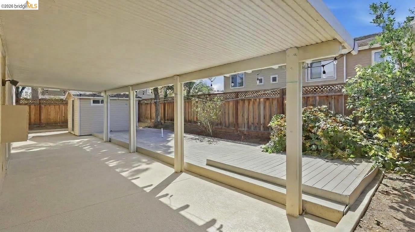 Covered backyard patio and raised deck with wooden fencing and shrubs.