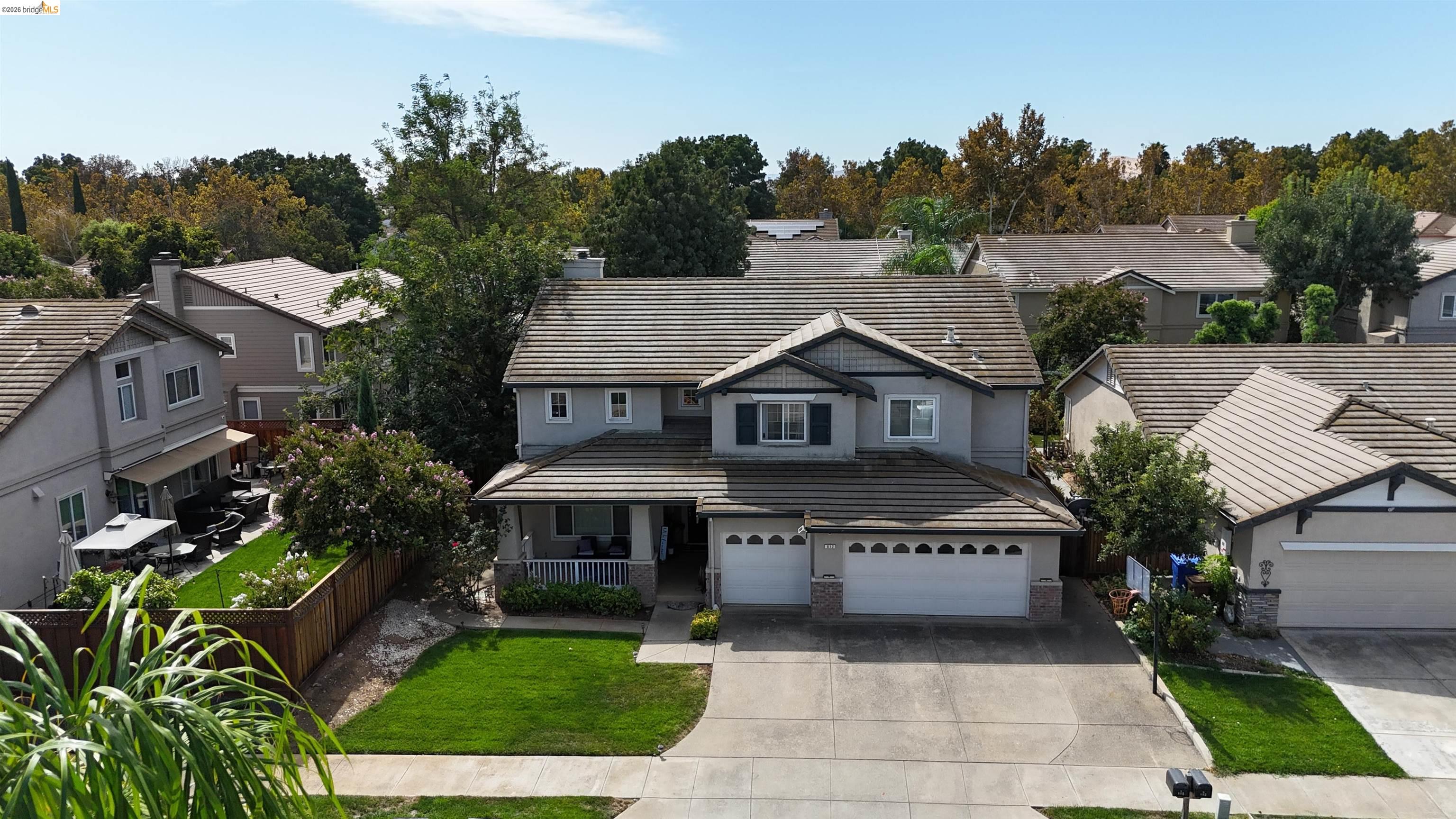 Gray two-story home with a tiled roof, two-car garage, and landscaped front yard, viewed from above.