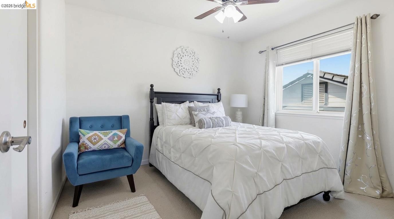 Bedroom with a white bed and blue accent chair beside a curtained window.